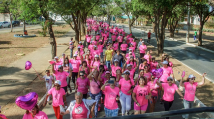 Pessoas realizando uma caminhada, usando uma camisa rosa, em concientização do Outubro Rosa